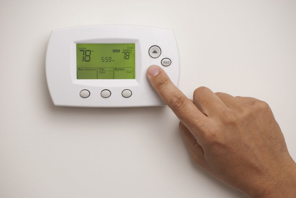 A person's hand adjusting the temperature control panel on a wall.