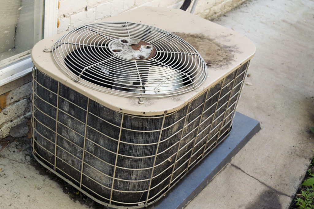 An old air conditioner unit, in need of updating, sitting in tall weeds