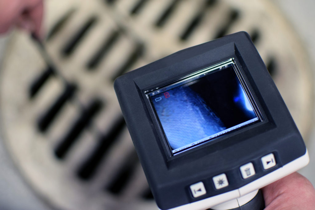 A technician holding a video camera inspection over a drain