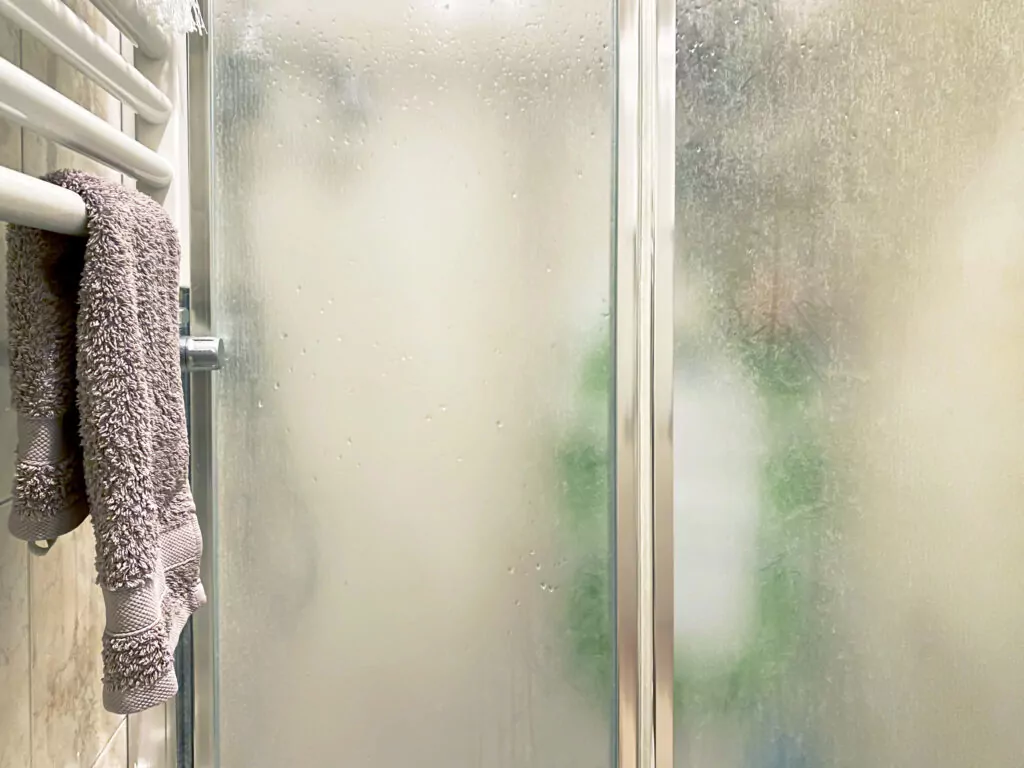 violet colored towel laid out on a white radiator near the shower enclosure with frosted glass doors and aluminum structure inside a bathroom