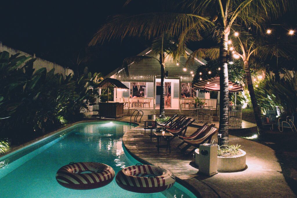 A backyard pool with string lights, pool lights, and security lights