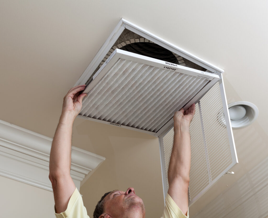 male reaching up to check air filter for HVAC ductwork