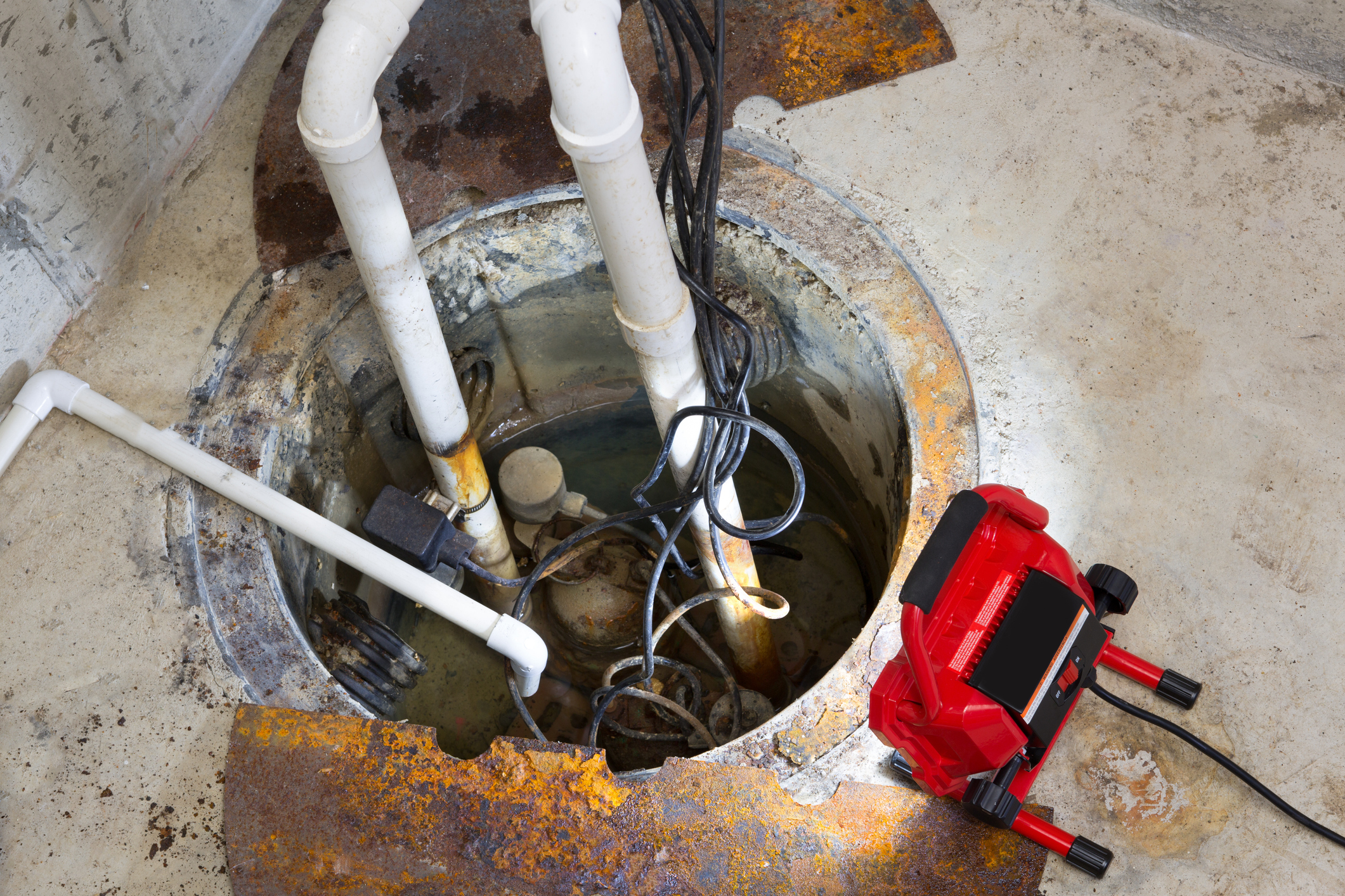 Repairing a sump pump in a basement with a red LED light illuminating the pit and pipe work for draining ground water