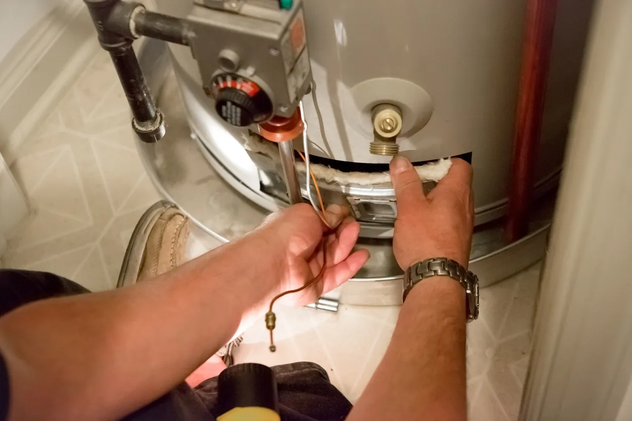 a man uses a flashlight to help him see the water heater in a dark closet