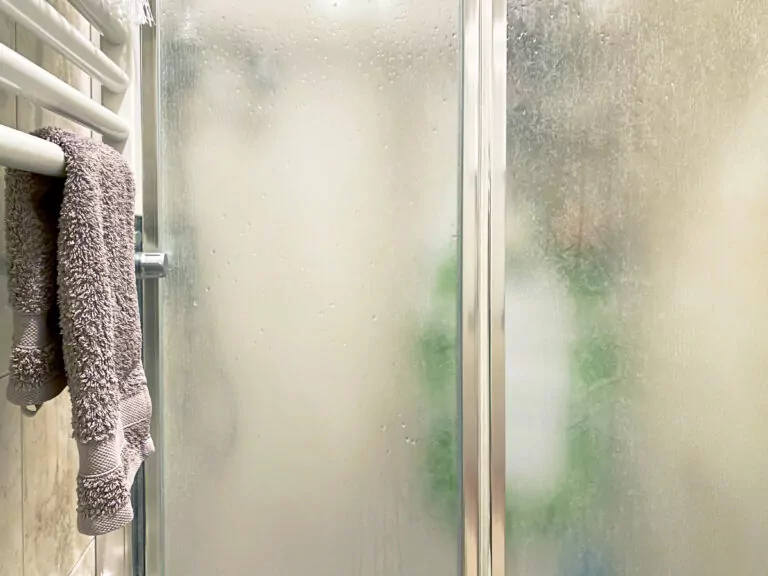 violet colored towel laid out on a white radiator near the shower enclosure with frosted glass doors and aluminum structure inside a bathroom