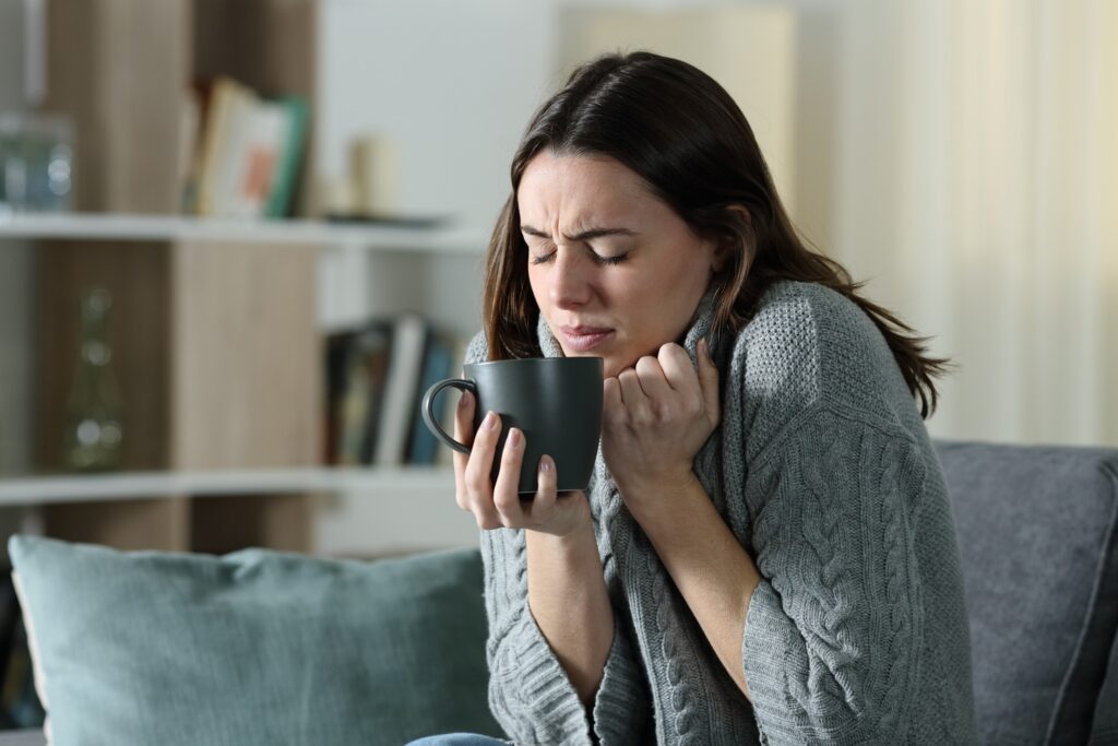 Woman getting cold holding coffee mug at home