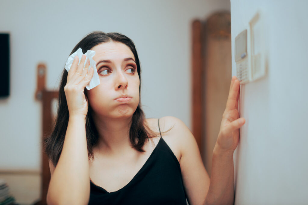 Woman blotting sweat from her forehead while adjusting the thermostat